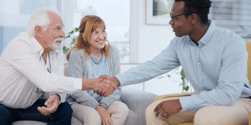 Older couple meeting and shaking hands with younger man while touring assisted living community