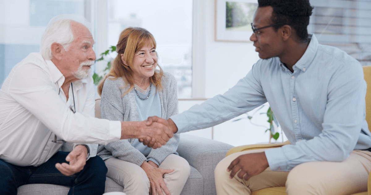 Older couple meeting and shaking hands with younger man while touring assisted living community