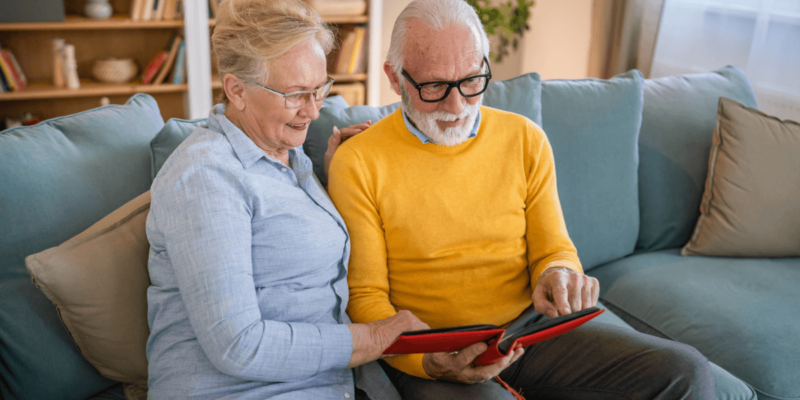 Senior woman and man sitting on couch looking through photo album.