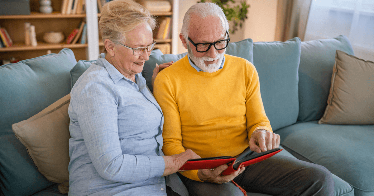 Senior woman and man sitting on couch looking through photo album.