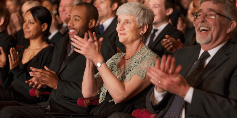 A crowd at a performance narrowed in on a elder woman clapping at Clearwater's Arts.